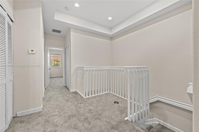 hall featuring light carpet, baseboards, visible vents, a tray ceiling, and recessed lighting