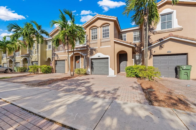 townhome / multi-family property with a garage, a tile roof, driveway, and stucco siding