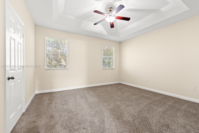 unfurnished room with carpet floors, a tray ceiling, ceiling fan, and baseboards