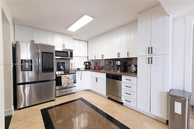 kitchen featuring dark countertops, decorative backsplash, appliances with stainless steel finishes, white cabinetry, and a sink