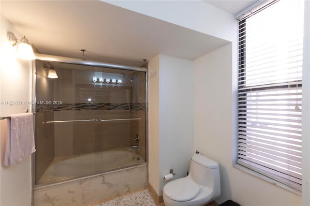 bathroom featuring toilet and shower / bath combination with glass door