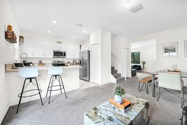 kitchen with light colored carpet, stainless steel appliances, visible vents, light countertops, and a kitchen bar