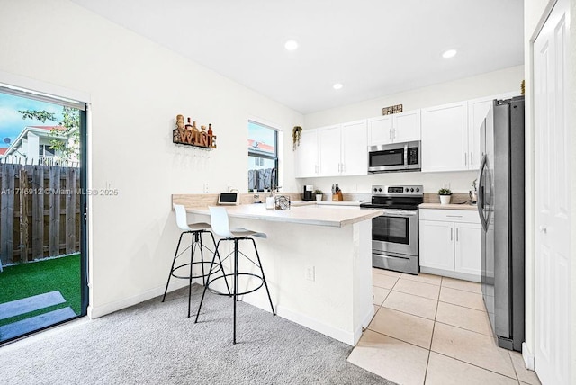 kitchen featuring light countertops, appliances with stainless steel finishes, white cabinets, a peninsula, and a kitchen breakfast bar