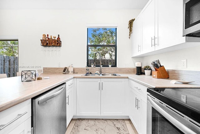 kitchen with stainless steel appliances, light countertops, a sink, and white cabinetry