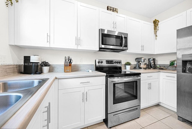 kitchen featuring stainless steel appliances, light countertops, a sink, and white cabinetry