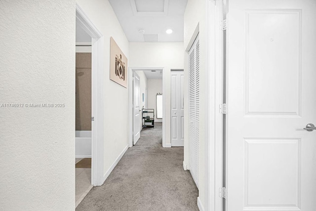 hallway with baseboards, attic access, and light colored carpet