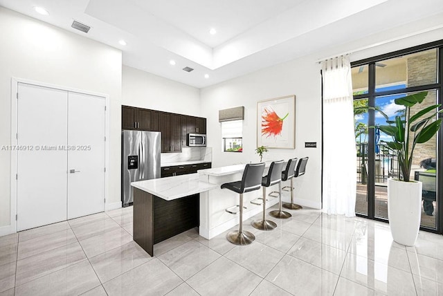 kitchen with dark brown cabinetry, visible vents, a kitchen island, appliances with stainless steel finishes, and a breakfast bar