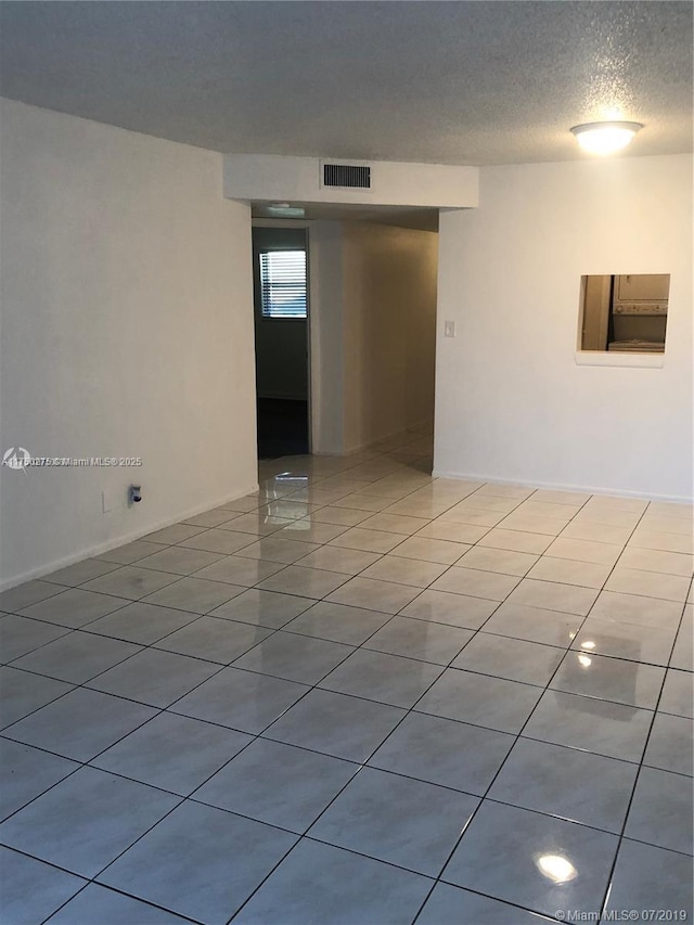 empty room with visible vents, a textured ceiling, and light tile patterned floors