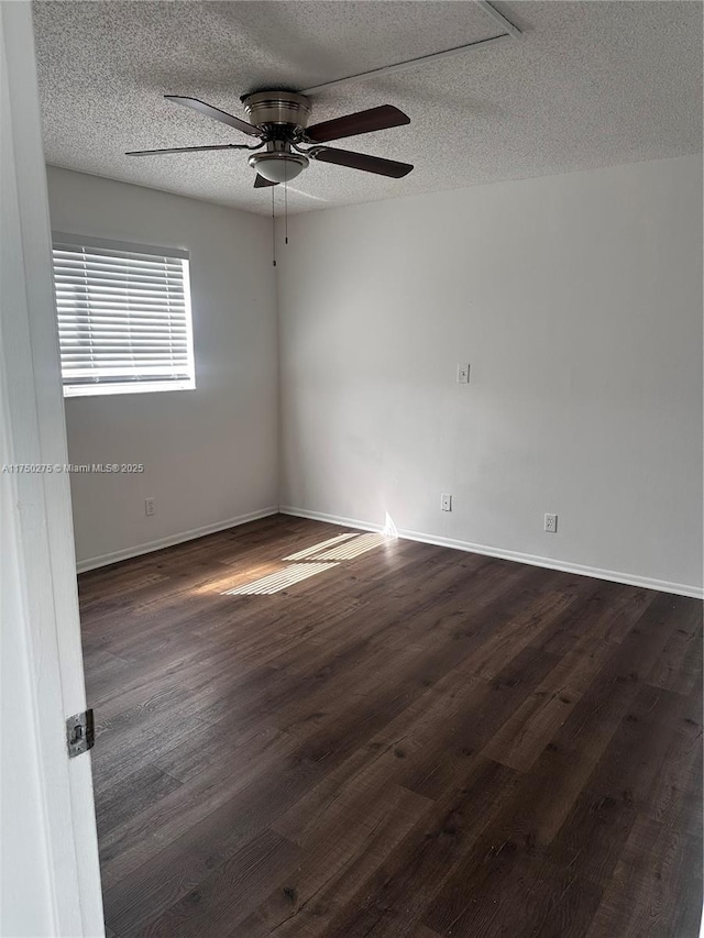 empty room with a textured ceiling, dark wood finished floors, a ceiling fan, and baseboards