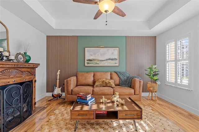 living area with a tray ceiling, a fireplace, and light wood-style flooring