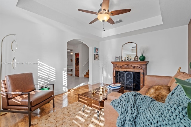 living room featuring arched walkways, a fireplace, a raised ceiling, visible vents, and light wood-style floors