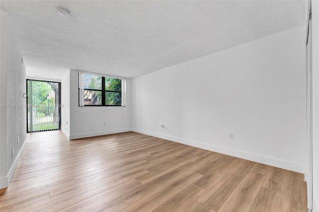 spare room with light wood-style flooring, baseboards, and a textured ceiling