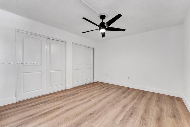 unfurnished bedroom with light wood finished floors, ceiling fan, baseboards, and multiple closets