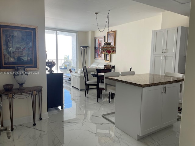 kitchen with baseboards, white cabinets, dark countertops, a kitchen island, and marble finish floor