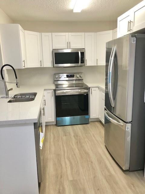 kitchen featuring stainless steel appliances, white cabinetry, a sink, and light wood-style flooring