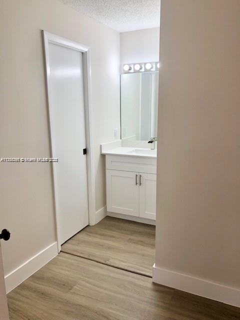 bathroom with a textured ceiling, wood finished floors, vanity, and baseboards