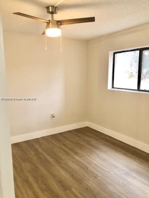 empty room featuring dark wood-style floors, a textured ceiling, a ceiling fan, and baseboards