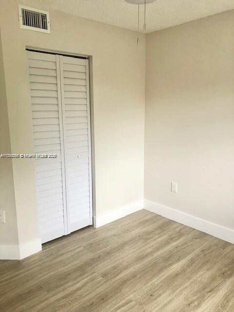 unfurnished bedroom with visible vents, a textured ceiling, baseboards, and wood finished floors