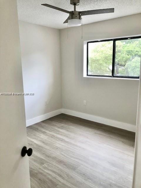 unfurnished room with a textured ceiling, wood finished floors, and baseboards