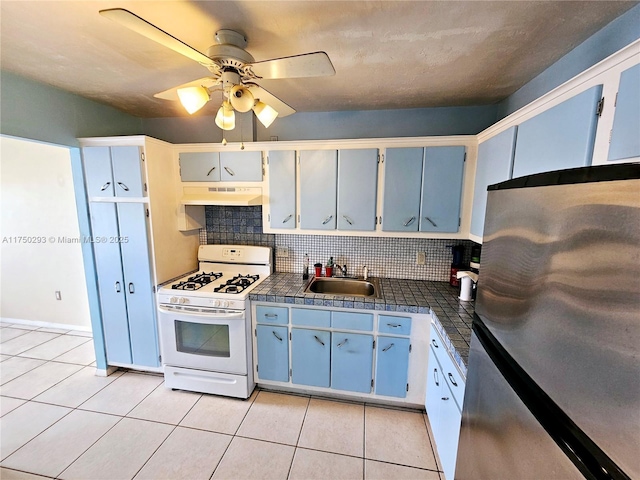 kitchen featuring light tile patterned floors, white gas stove, under cabinet range hood, tile counters, and freestanding refrigerator