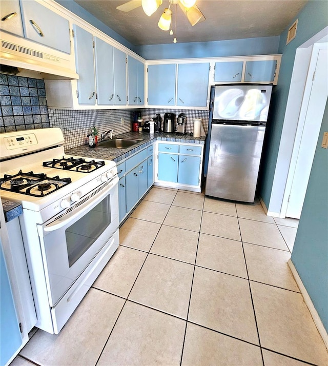 kitchen with freestanding refrigerator, light tile patterned flooring, white range with gas cooktop, a sink, and under cabinet range hood