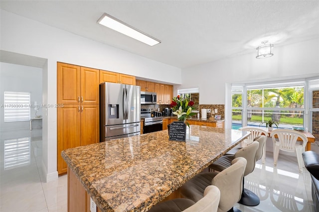 kitchen featuring stainless steel appliances, stone countertops, backsplash, and a kitchen bar