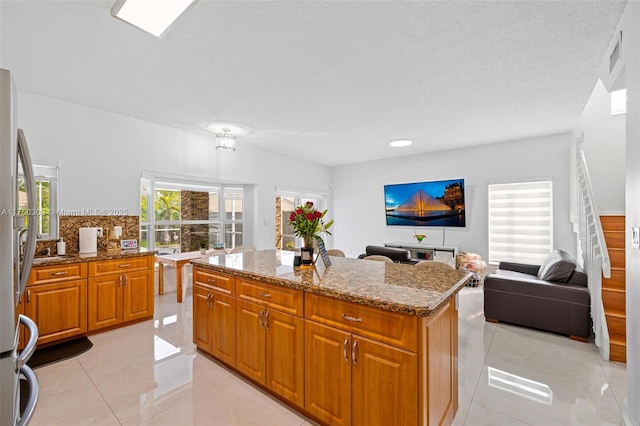 kitchen with open floor plan, stone countertops, a kitchen island, and brown cabinets