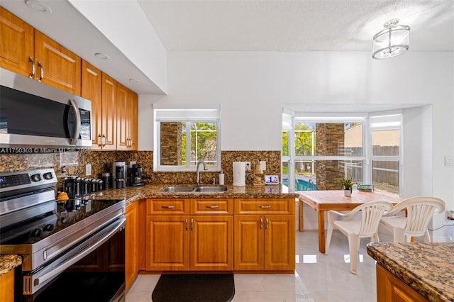 kitchen featuring brown cabinets, tasteful backsplash, appliances with stainless steel finishes, a sink, and dark stone counters