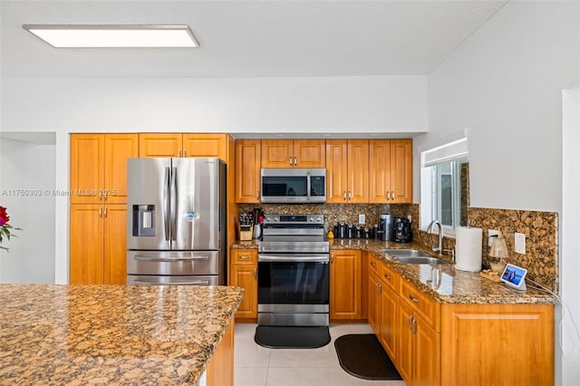 kitchen with decorative backsplash, dark stone counters, brown cabinets, stainless steel appliances, and a sink