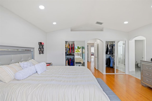 bedroom with arched walkways, two closets, lofted ceiling, visible vents, and light wood-type flooring