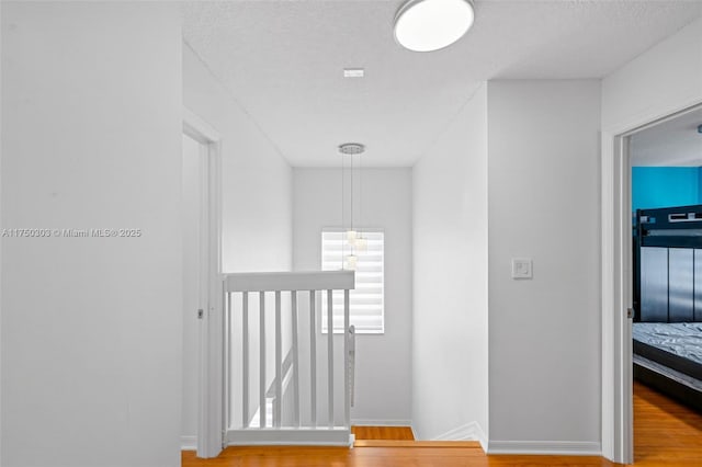 corridor featuring an upstairs landing, a textured ceiling, baseboards, and wood finished floors