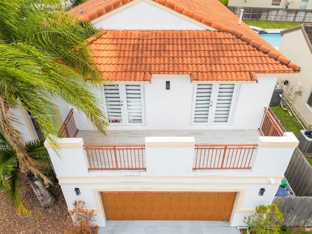 exterior space featuring an attached garage, a balcony, fence, a tiled roof, and stucco siding