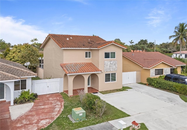 mediterranean / spanish-style home featuring stucco siding, concrete driveway, a gate, fence, and a tiled roof