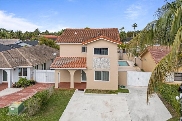 mediterranean / spanish-style home with a gate, a tile roof, a fenced backyard, and stucco siding