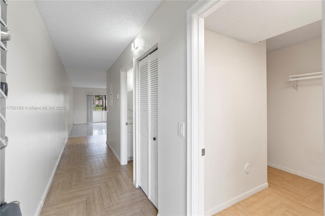 hall featuring a textured ceiling and baseboards