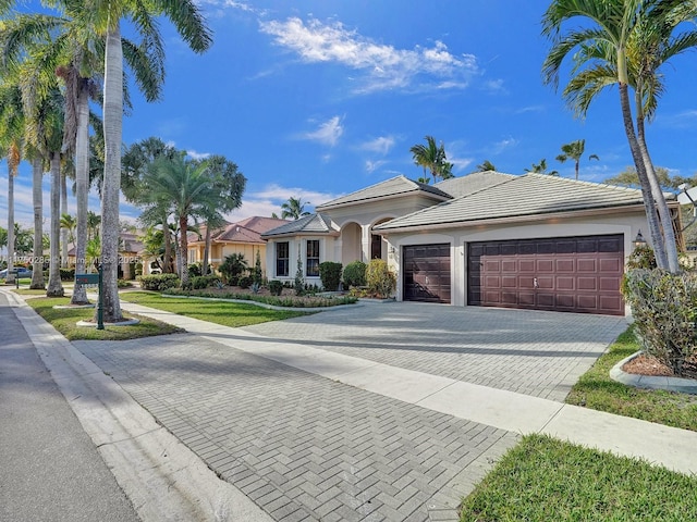 view of front facade with stucco siding, a front lawn, a garage, a tile roof, and decorative driveway