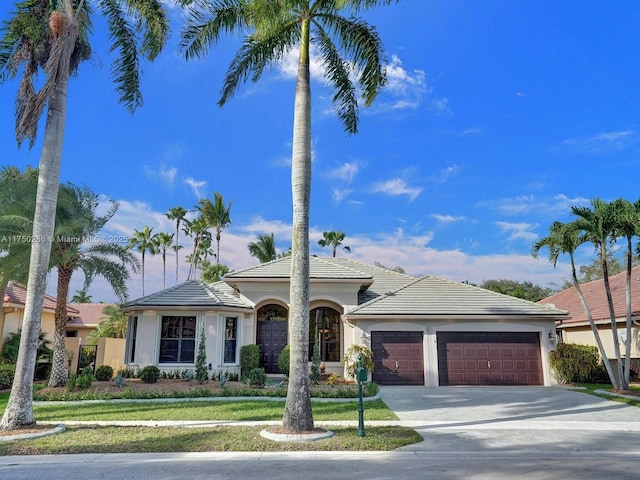 view of front of home featuring a tile roof, stucco siding, a garage, driveway, and a front lawn