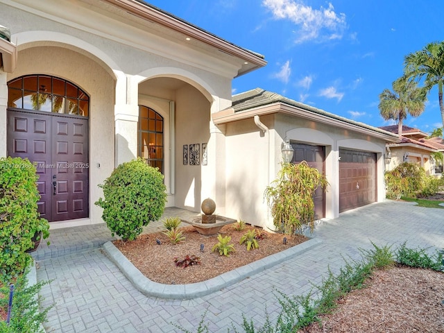 property entrance with a garage, decorative driveway, and stucco siding