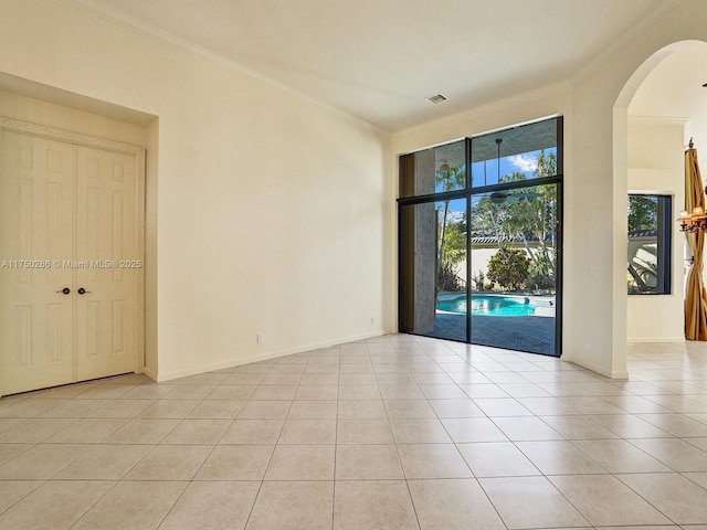 spare room with baseboards, visible vents, arched walkways, ornamental molding, and light tile patterned flooring