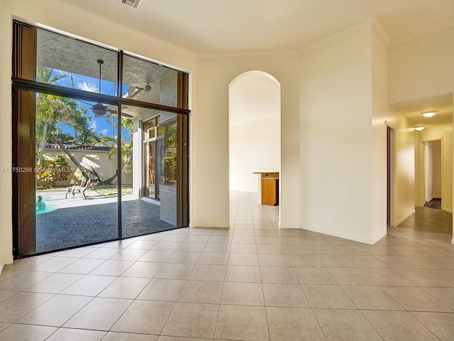 empty room featuring arched walkways, crown molding, and light tile patterned floors