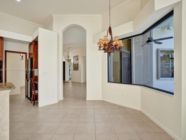 empty room featuring light tile patterned floors, arched walkways, ceiling fan with notable chandelier, baseboards, and crown molding