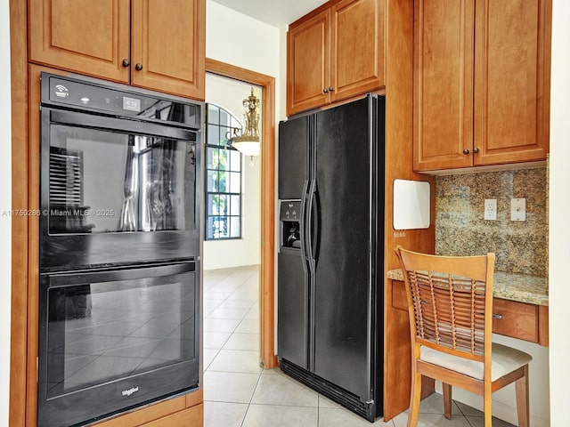 kitchen with light tile patterned floors, built in study area, brown cabinets, black appliances, and tasteful backsplash