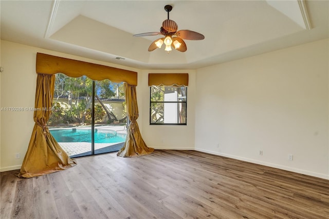 spare room featuring wood finished floors, a raised ceiling, a ceiling fan, and baseboards