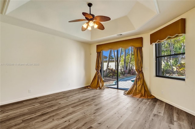 unfurnished room with wood finished floors, a ceiling fan, visible vents, baseboards, and a tray ceiling