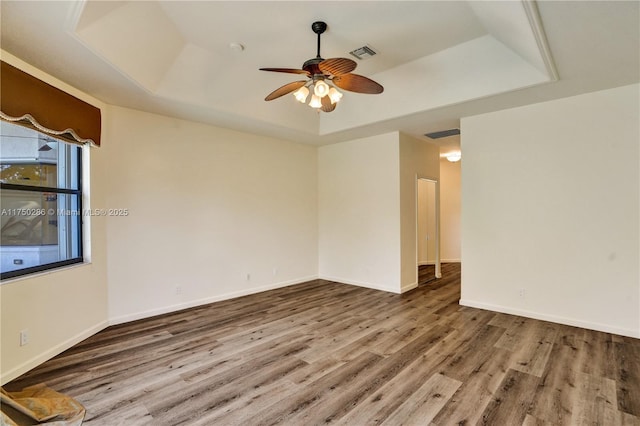 unfurnished room featuring ceiling fan, wood finished floors, visible vents, baseboards, and a raised ceiling