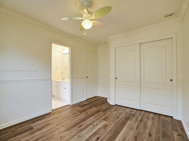 unfurnished bedroom with a sink, wood finished floors, visible vents, a closet, and crown molding