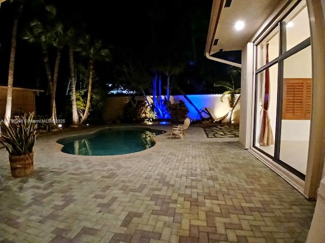 pool at night featuring a patio area and an outdoor pool