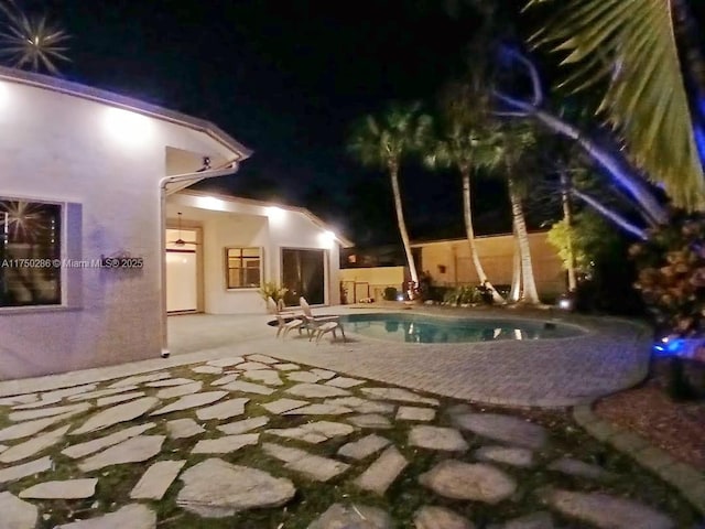 pool at night featuring a fenced in pool and a patio area