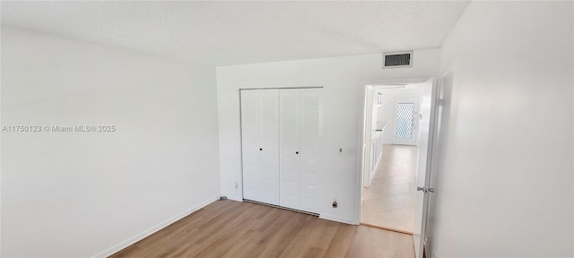 unfurnished bedroom featuring a closet, visible vents, a textured ceiling, light wood-type flooring, and baseboards