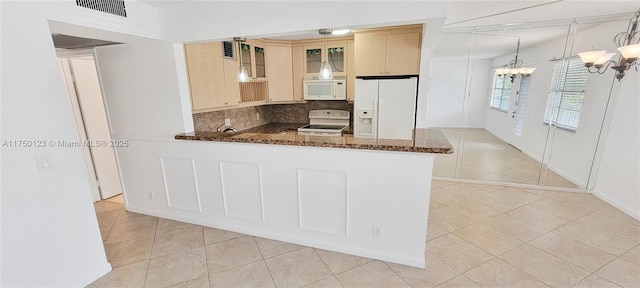 kitchen with pendant lighting, glass insert cabinets, dark stone countertops, white appliances, and a peninsula